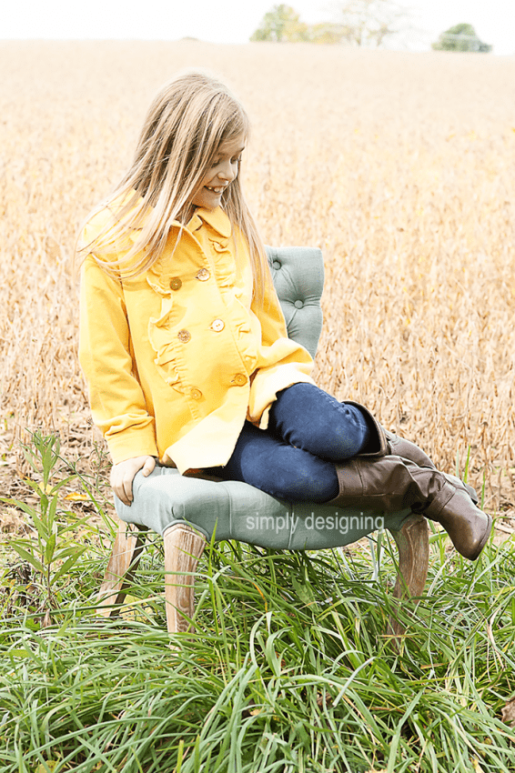 Photo of a young Girl on Chair with her legs bent up beside her on the seat. This family photo was taken in a field of wheat and grass