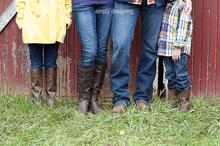 Photo of mom, dad and 2 kids from the waist down in boots standing in grass in front of a barn door