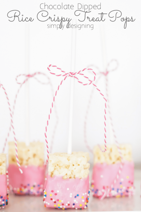 close up of pink Chocolate Dipped Rice Crispy Treat Pops standing up with sticks in the air and a pink twine bow tied to the stick