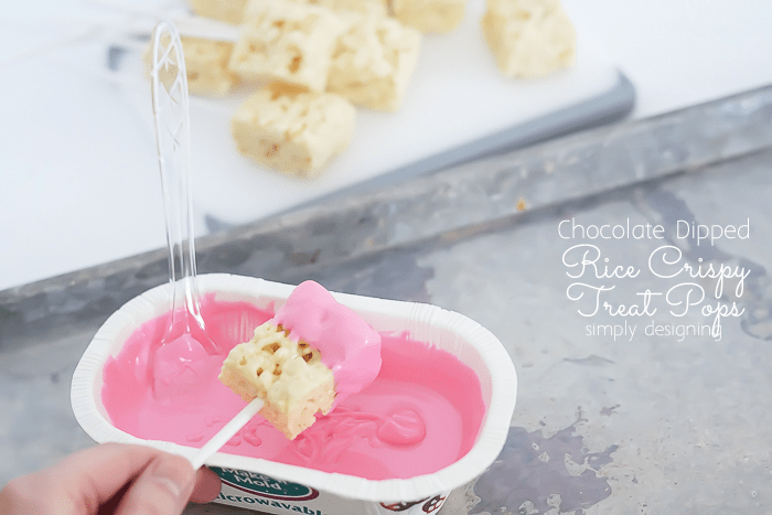 Diping Rice Crispy Treats in pink melted chocolate covering ½ of the Rice Krispy Treat