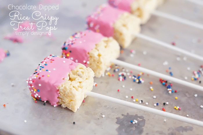 Rice Crispy Treat Pops that were dipped in pink chocolate and sprinkled with candy sprinkles laying on wax paper to harden
