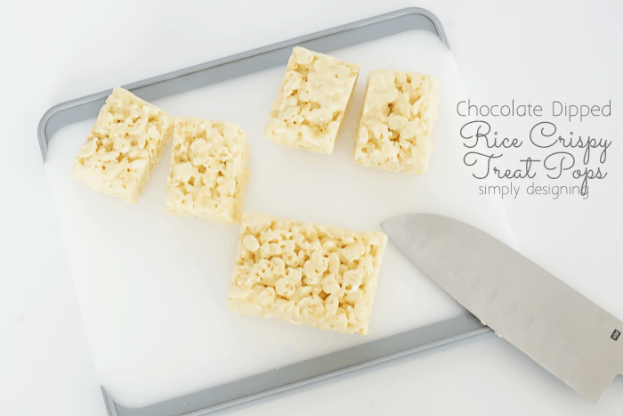 rectangle Rice Krispy Treats on a cutting board being cut in half with a knife