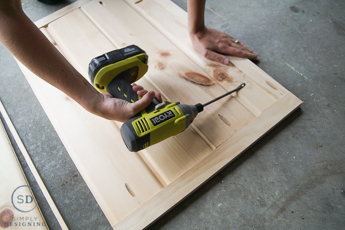 Using a drill to screw into pocket holes to attach the car siding boards to the outer 1"x2" frame.