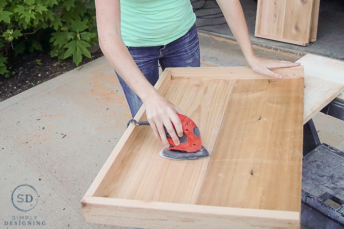 Ashley from Simply Designing using an electric sander to sand the shelves down for the printer table