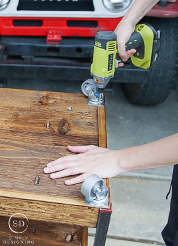 Using a drill to attach casters to the bottom of the DIY Printer Table