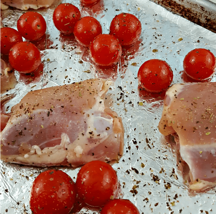 Simple to prep Sheet Pan Caprese Chicken - chicken breasts on a tinfoil lined sheet pan with tomatoes sprinkled with olive oil and Italian seasoning.