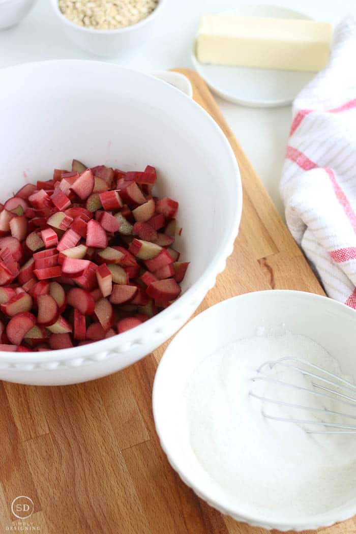 Chopped rhubarb in a mixing bowl alongside a bowl with whisked sugar