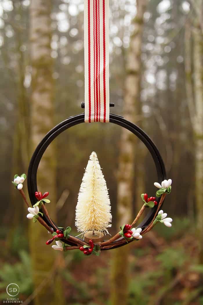 farmhouse ornament hanging in front of forest trees