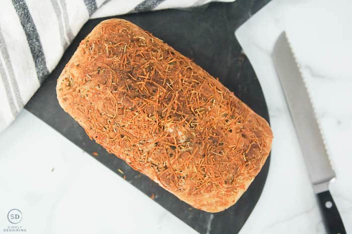 rosemary parmesan bread baked not sliced on marble board with knife on side