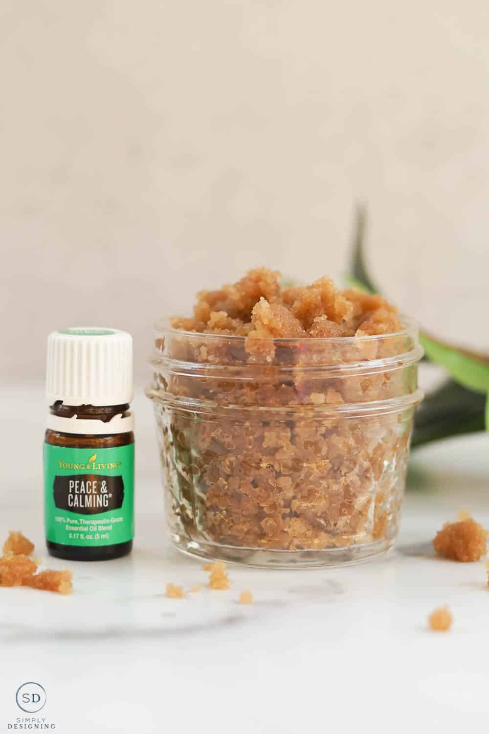 homemade brown sugar scrub in a small ball glass jar with peace and calming esential oil and greenery in the background