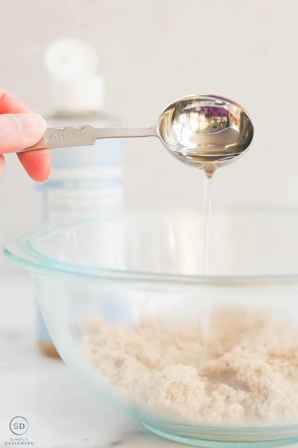 pouring castile soap into bowl with measuring spoon