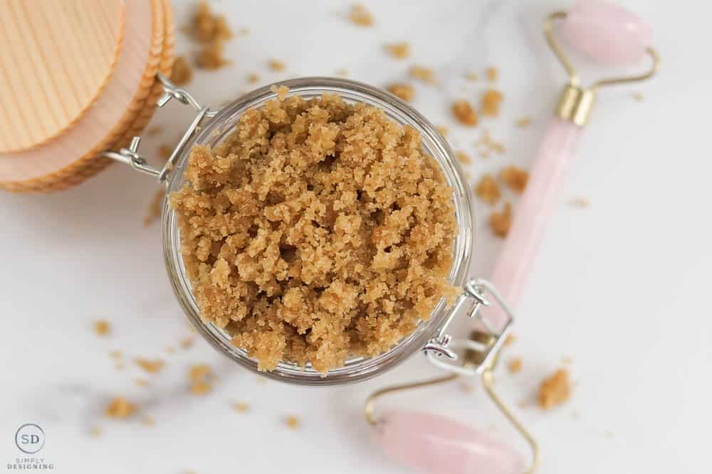 horizontal image of brown sugar face scrub DIY looking from the top down in a glas jar with a wood lid and a pink face roller