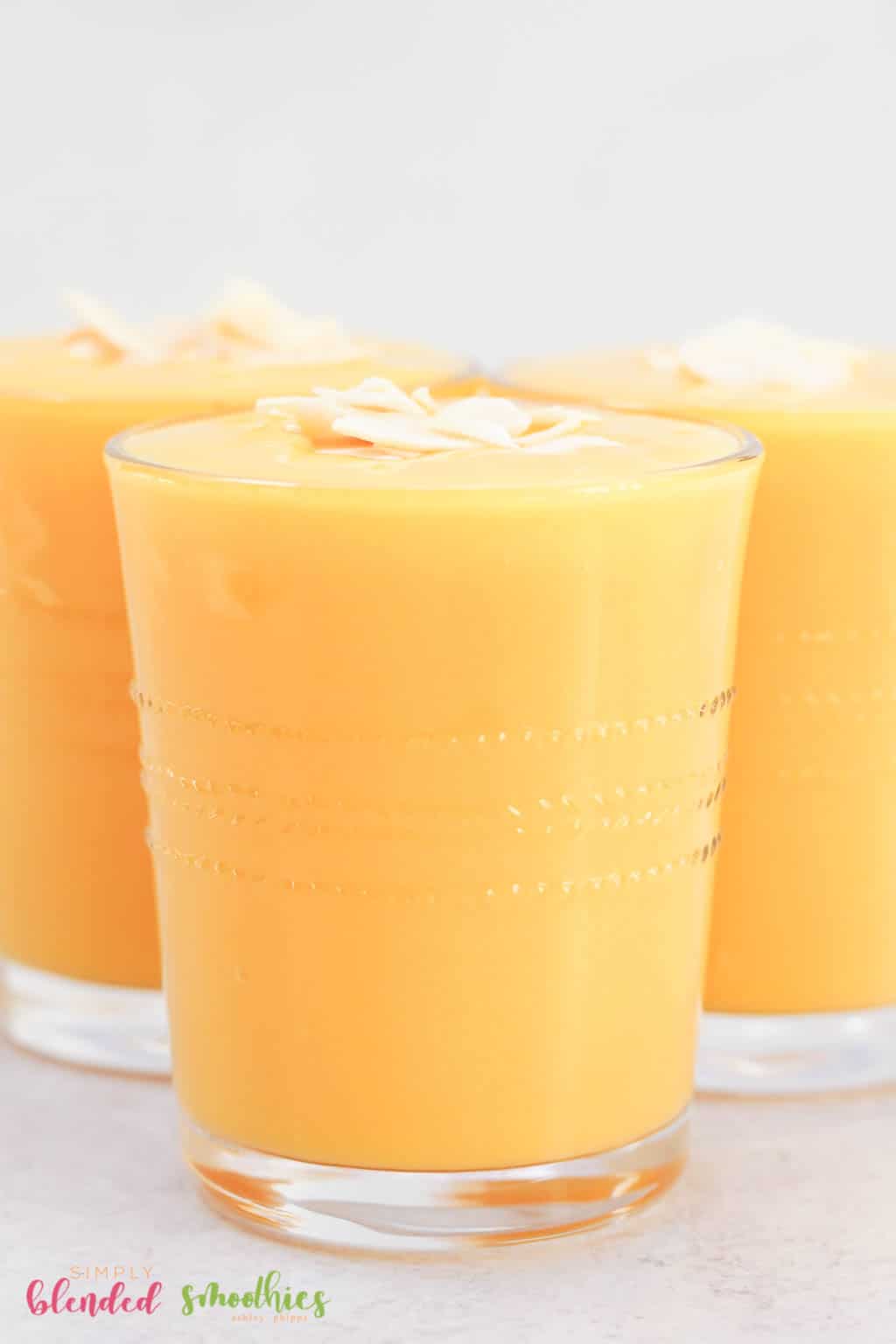 Peach Pineapple Smoothie 11 Close up vertical photo of mango peach smoothie in a clean glass with coconut flakes on top