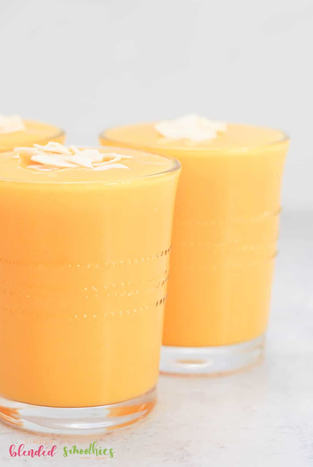 Mango Peach Smoothie 3 side view of smoothie made with mangos and peaches topped with coconut flakes in a clear glass