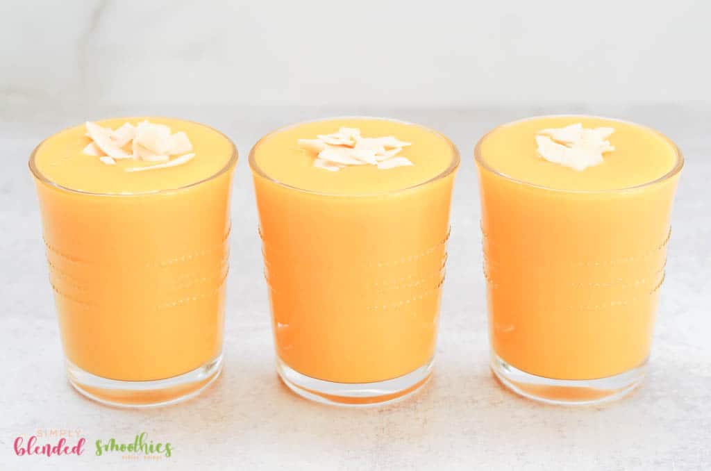 Mango Peach Smoothie 4 three smoothies lined up next to each other - mango peach smoothies with coconut flakes on top in clear glasses