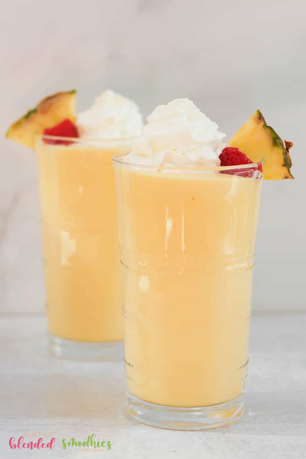 Banana Peach Smoothie 18 vertical photo of two pineapple peach milkshakes topped with a pineapple slice raspberry and whipped cream