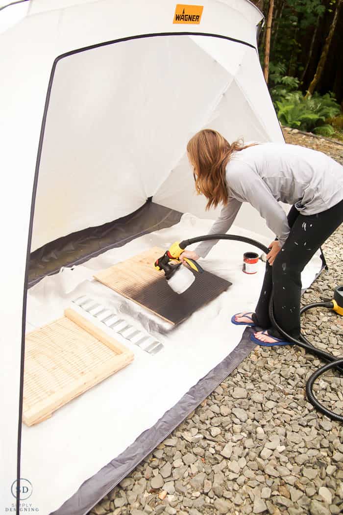 woman spraying bat houses in spray shelter with paint sprayer