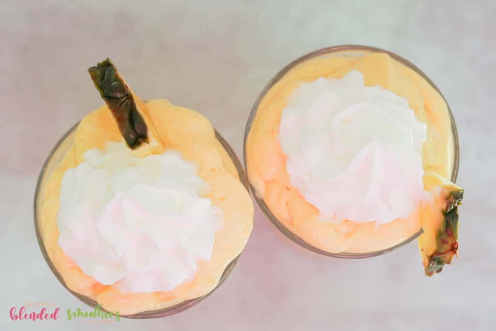 Mango Pineapple Milkshake 2 milkshake made with pineapple and mango look at it from the top down topped with whipped cream and fresh pineapple slice
