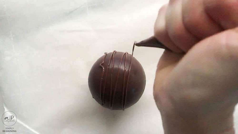 use a decorating bag and melted chocolate to decorate hot cocoa bombs